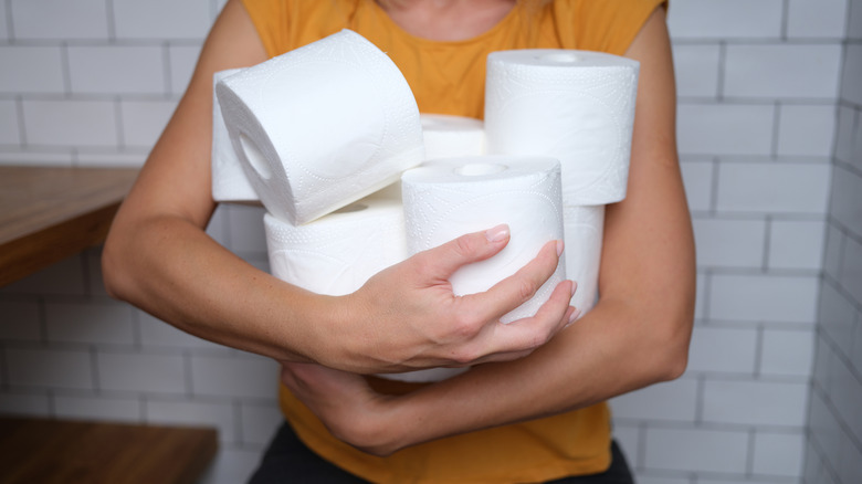 A person holding rolls of toilet paper in a bathroom