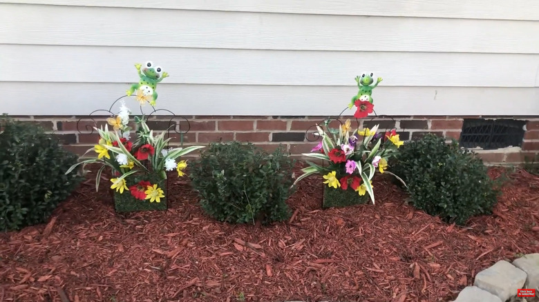 Two floral panels pushed into the ground in a landscaped bed near bushes