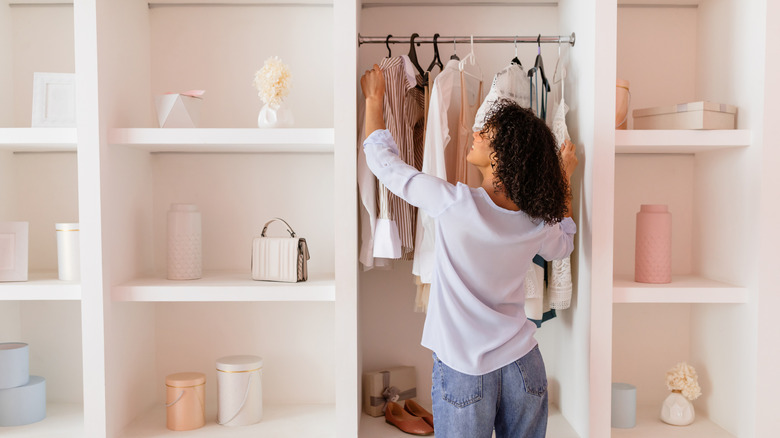Woman looking at clothes in a small built-in closet.