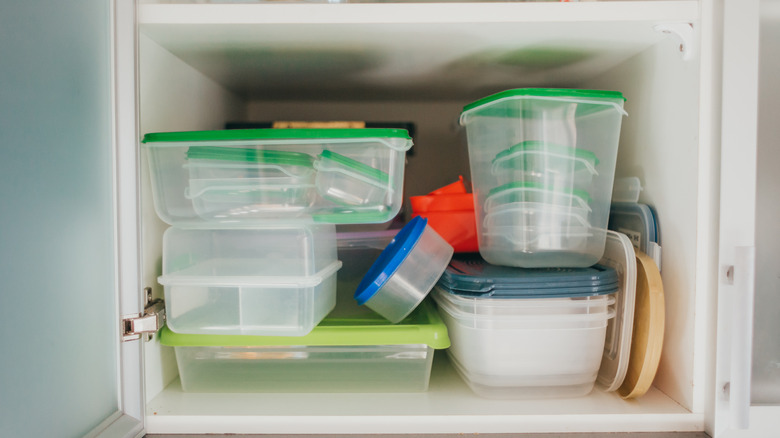 plastic tupperware food storage containers precariously perched in white kitchen cabinets