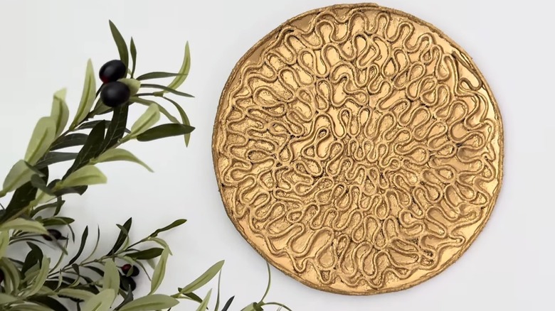 Pizza tin wall art covered in cotton cord, textured paint, and spray-painted gold