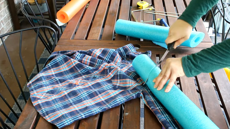 A woman cuts into a blue pool noodle over a plaid shirt