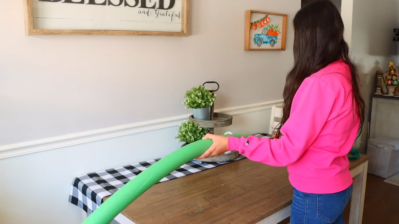 A woman folds a green pool noodle for a DIY project