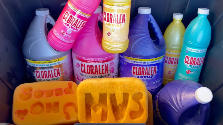 An assortment of colorful bottles of Cloralen Scented Bleach are arranged in a black tub