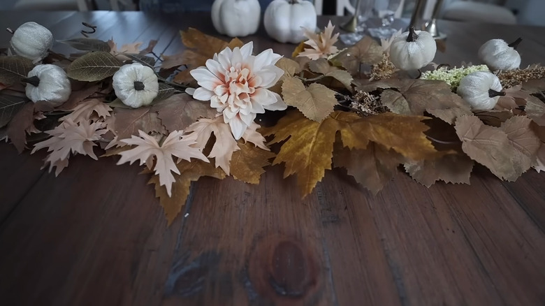 Fall-themed faux florals with white pumpkin accents sit on a wooden table