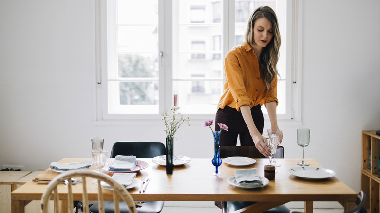 a young woman sets a dining room table