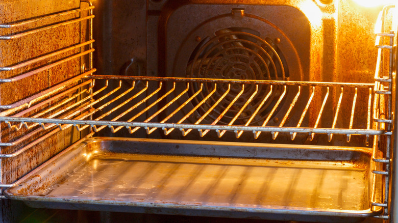 A baking sheet set underneath a rack in a lit oven.