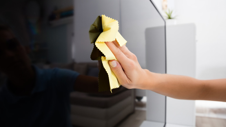 a hand cleans a television with a cloth