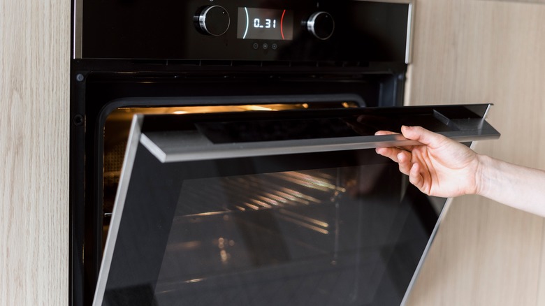 Shiny, clean glass oven door being opened by a hand