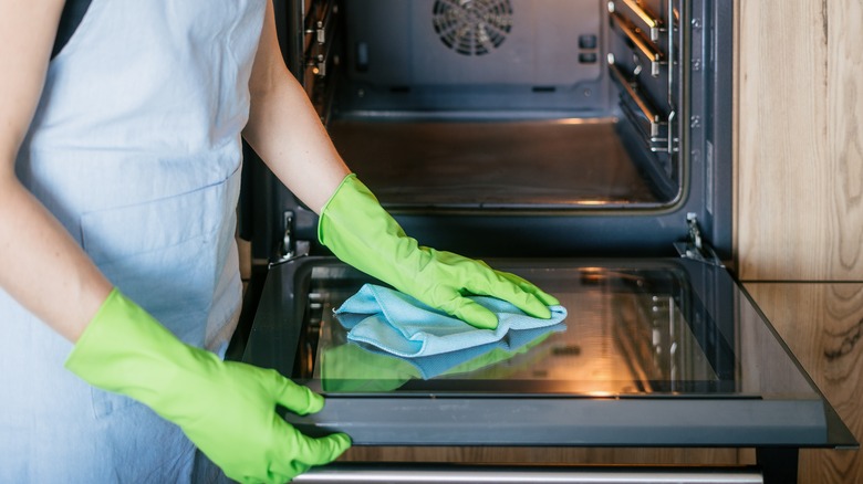 Gloved hands cleaning a glass oven door
