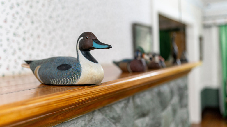 A duck decoy resting on a wooden mantle with others blurred in the background.