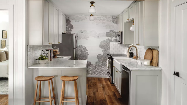 A kitchen with a white subway tile backsplash and an accent wall featuring a monochrome line art mural wallpaper