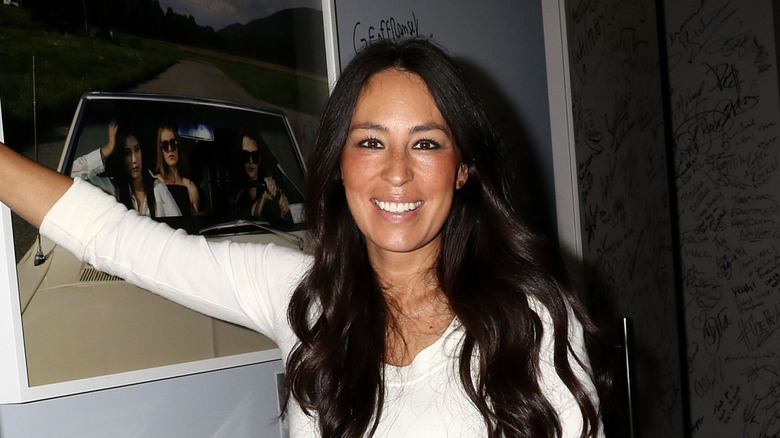 A headshot of a woman (Joanna Gaines) with long dark hair smiling at the camera