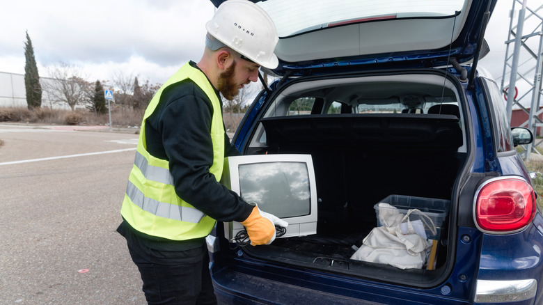 Man wearing a hard hat and recycling vest loading a tube TV into the back of a car