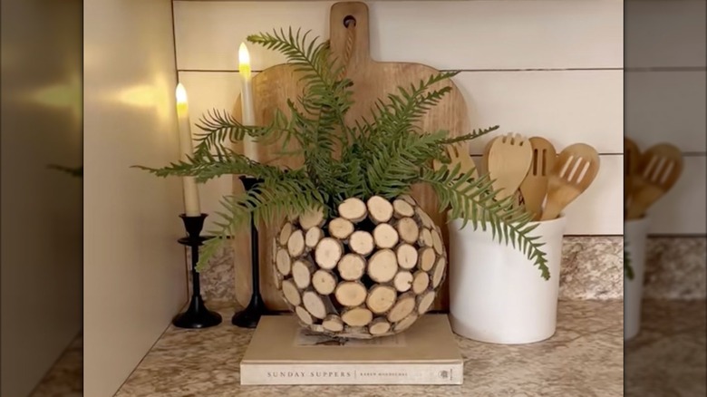 faux ferns fill a unique wooden vase surrounded by utensils on a kitchen countertop