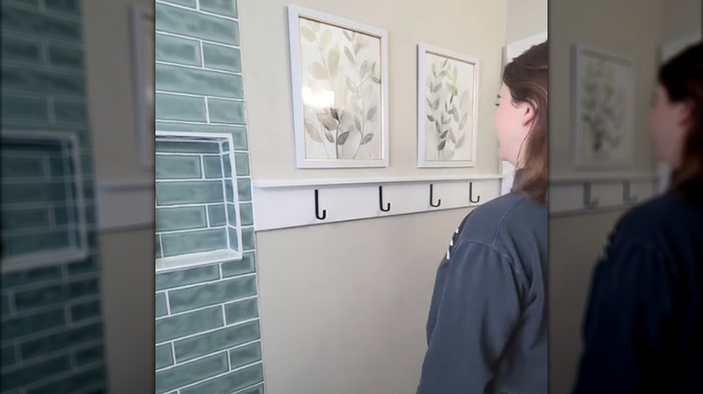 Smiling woman standing in front of DIY towel rack design with chic floral prints and subway-style tiles