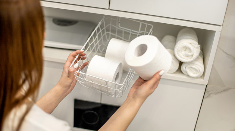 Young woman reaching for toilet paper in basket