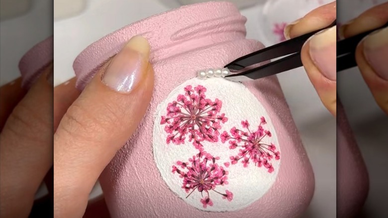 A person decorating a glass jar with paint, flowers, and pearls for spring