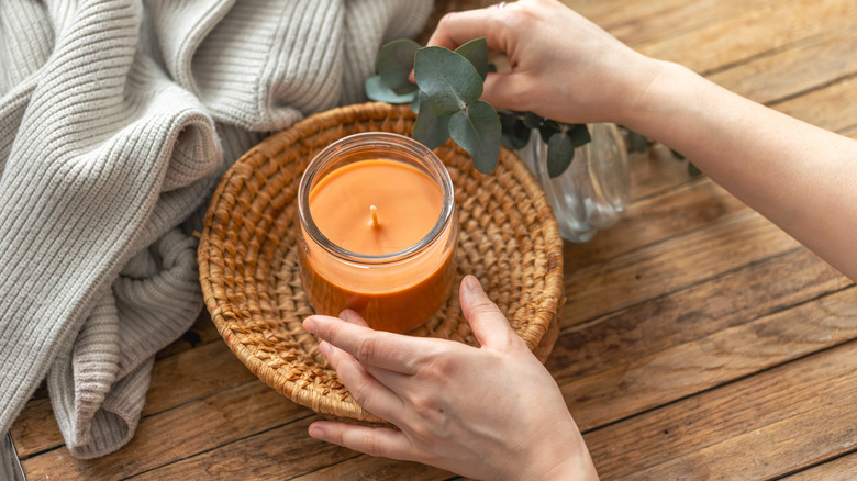 Person adjusting a jar candle on a basket with a blanket next to it