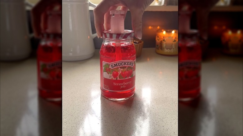 Person putting a pump lid on top of a strawberry jelly jar filled with reddish hand soap