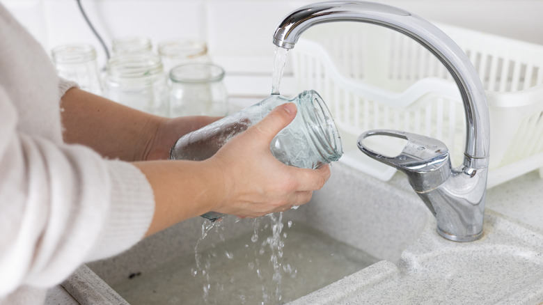 Person washing pasta sauce jar in sink