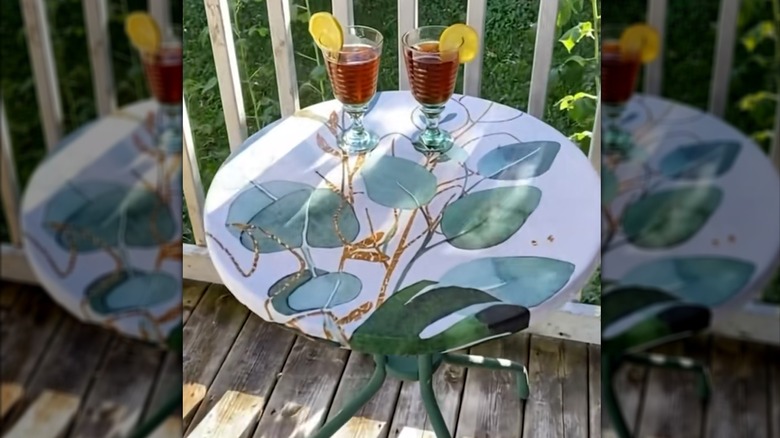 Outdoor table wrapped in curtain with gold and green leaf design with two glass goblets