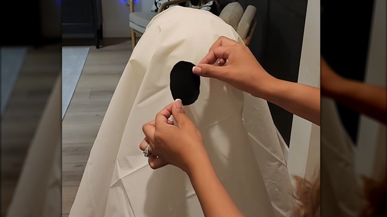 Woman attaching black cutout eye to white shower curtain ghost in house