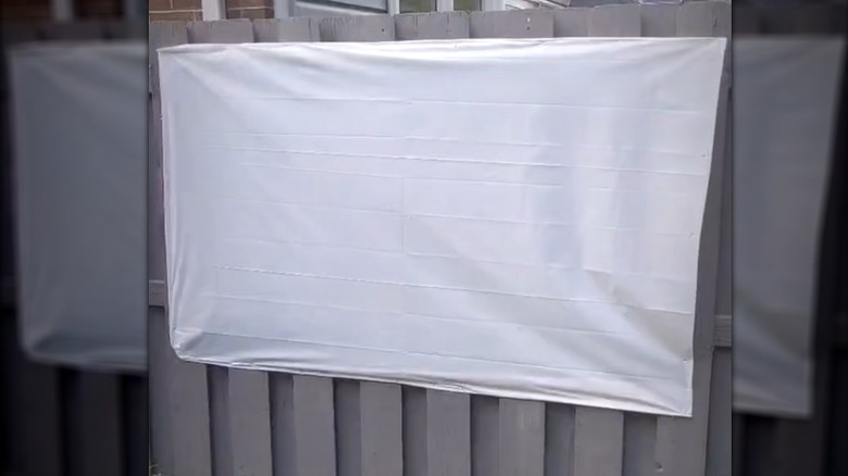 Plain white shower curtain stretched along outdoor fence as projector screen
