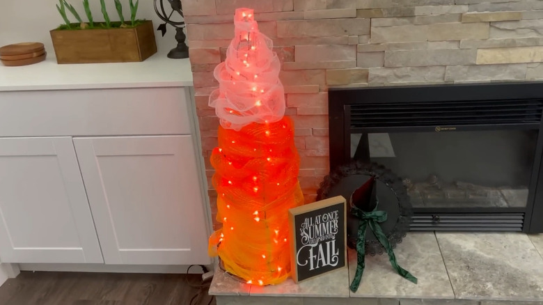Tomato cage wrapped in colorful fabric and lights, making it look like a piece of candycorn
