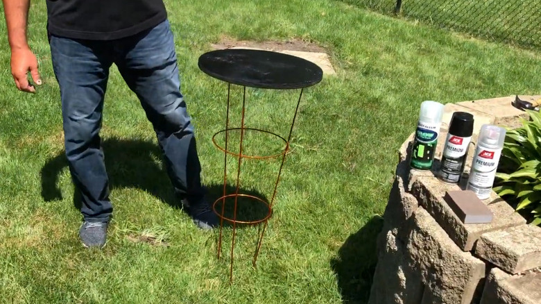 Man standing next to a DIY table made of a tomato cage and a wood