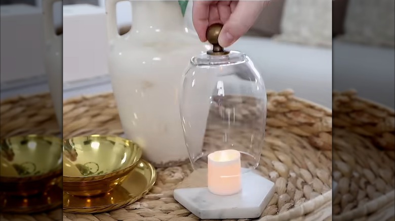 Hand holding a candle cloche over a lit candle