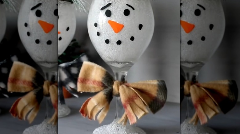 Snowman face drawn on a wine glass with a bow attached to the stem