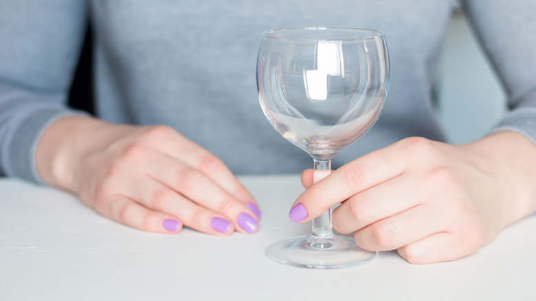 Hand holding an empty wine glass on a table