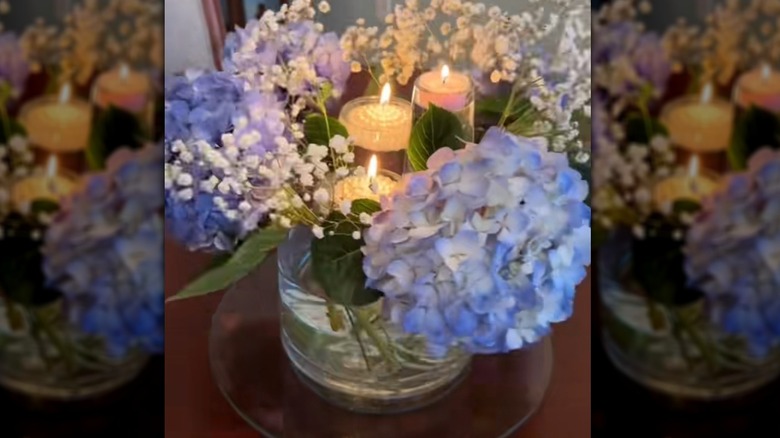 Flowers in a huge vase with lit candles inside wine glasses