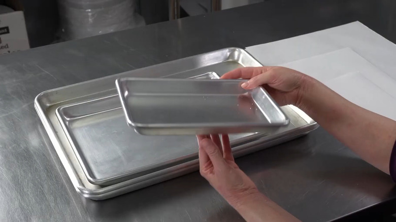 Person holding a small cake pan with larger pans in the background