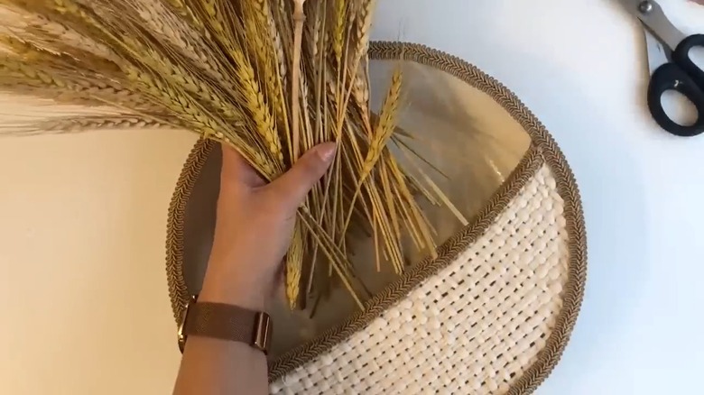 A person's hand tucking artificial grass into DIY wall decor made from old cooking pan and twine