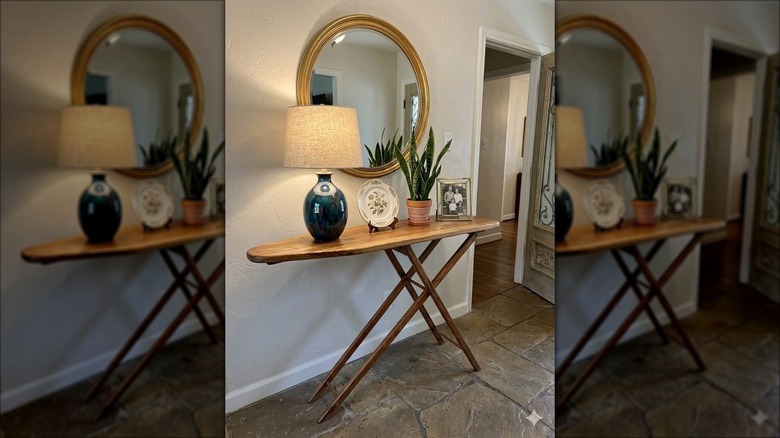 Wooden ironing board decorated with a lamp, plant, and other decor