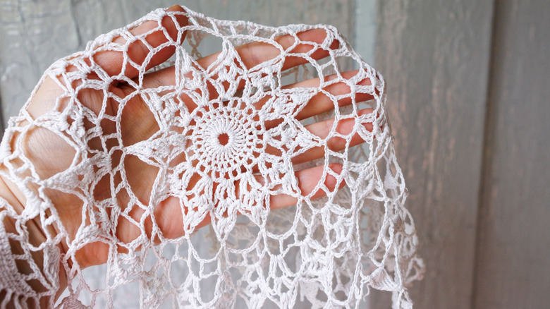 A hand holds up a vintage lace doily
