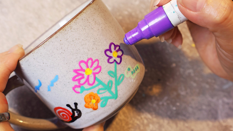 A person drawing with paint pens on a coffee mug