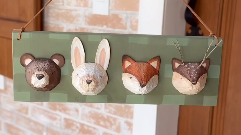 Four woodland creature faces painted on old egg carton cups are arranged on a plaid wooden board