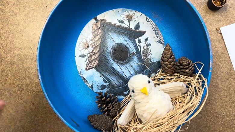 Upcycled whimsical frying pan with bird's nest and birdhouse design for home decor on crafting table surface