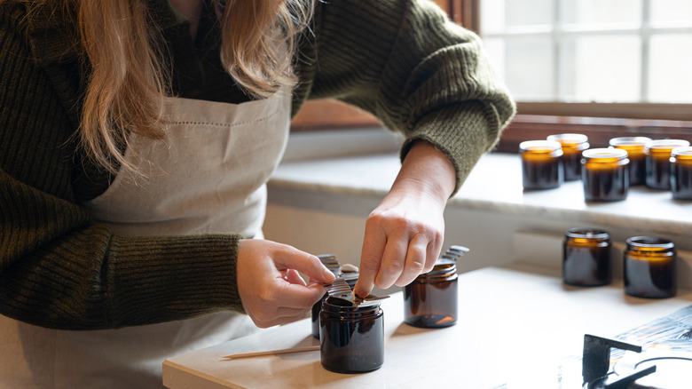 Woman placing a candle wick in a brown jar