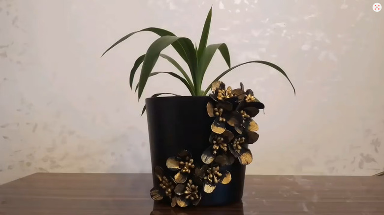 Gold egg carton flowers decorating a black planter with a plant in it