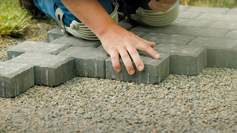 A hand placing pavers on ground