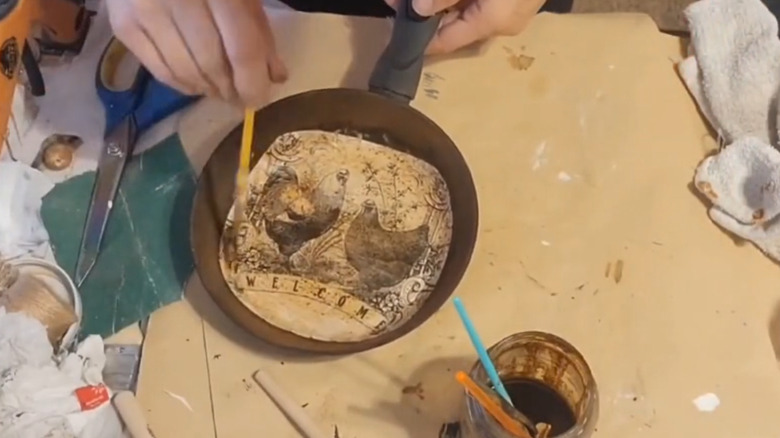 A woman brushing coffee over a decoupaged frying pan
