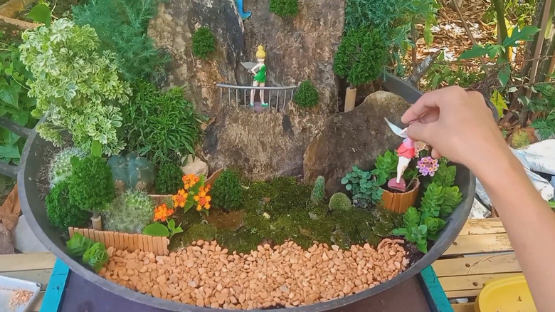 Person positioning mini fairies in a fairy garden made in a large skillet
