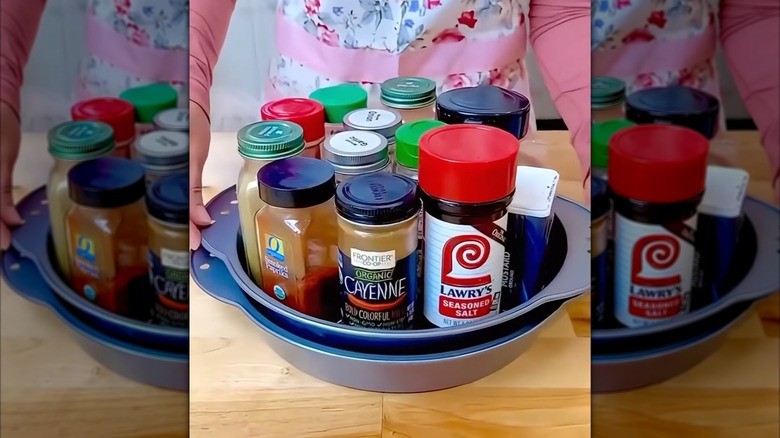 A person stands behind a cake pan lazy Susan filled with spices