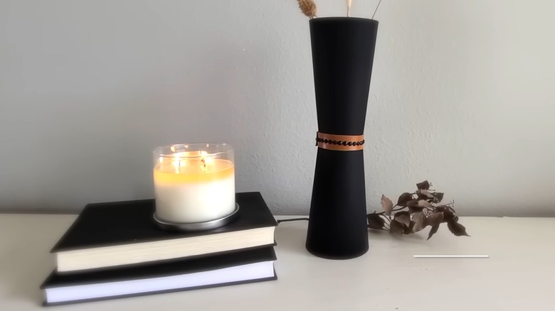 Stylish black DIY vase on white tabletop with candle and matching coffee table books with artificial foliage