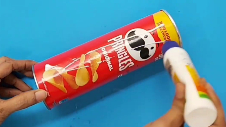 A person adds glue to a Pringles can