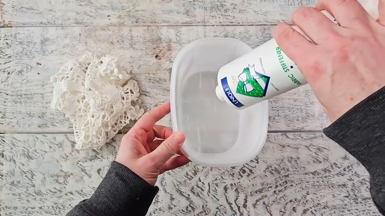 A person pours fabric stiffener in a bowl with a lace doily in the background